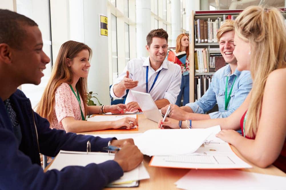 Group Of Students Working Together In Library With Teacher